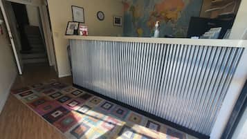 Une salle d'attente avec un tapis à motifs, une carte du monde accrochée au mur, des certificats encadrés et une horloge.