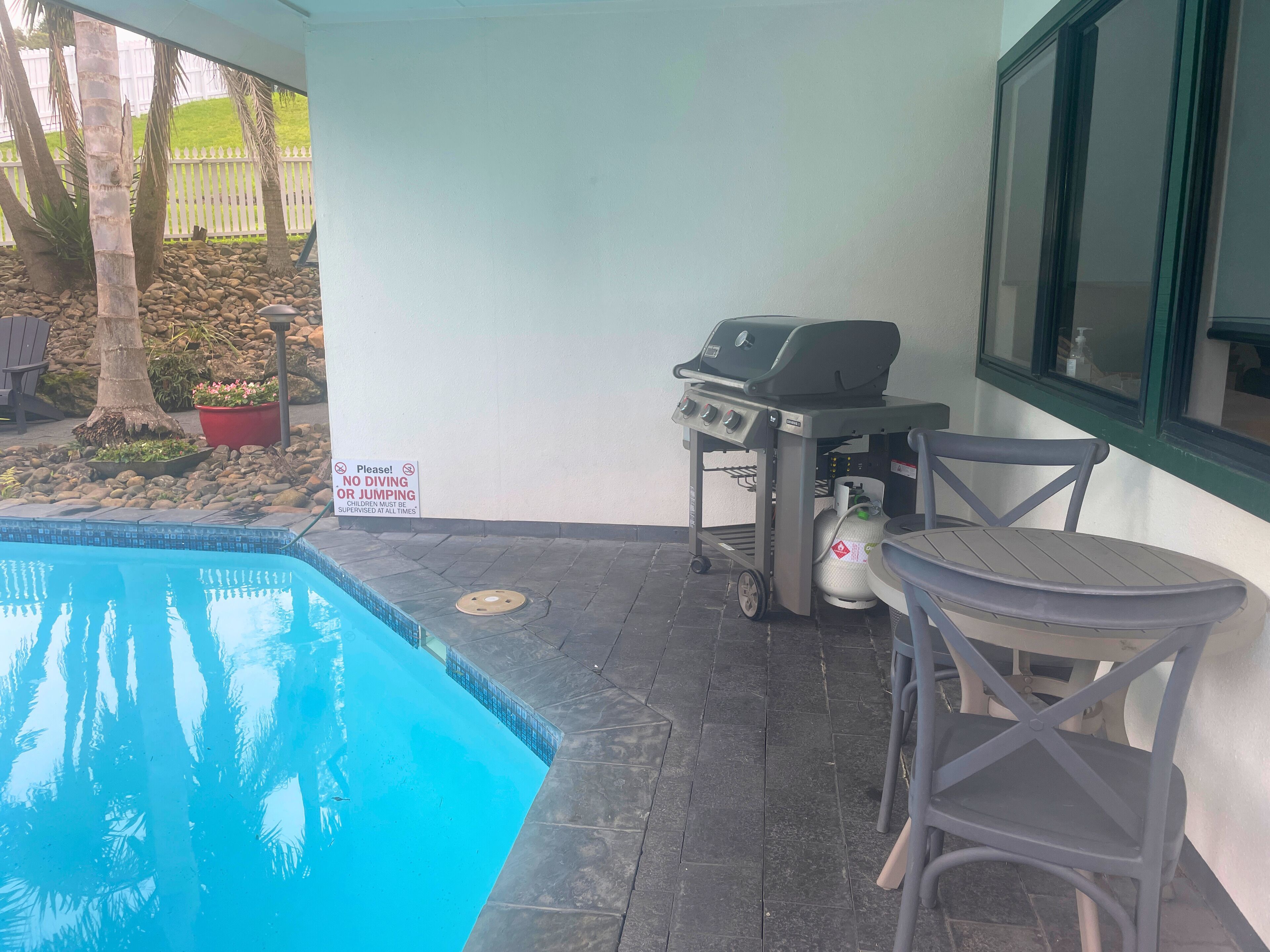 Un espace aménagé au bord de la piscine, comprenant un barbecue, une bouteille de gaz et une table avec des chaises.