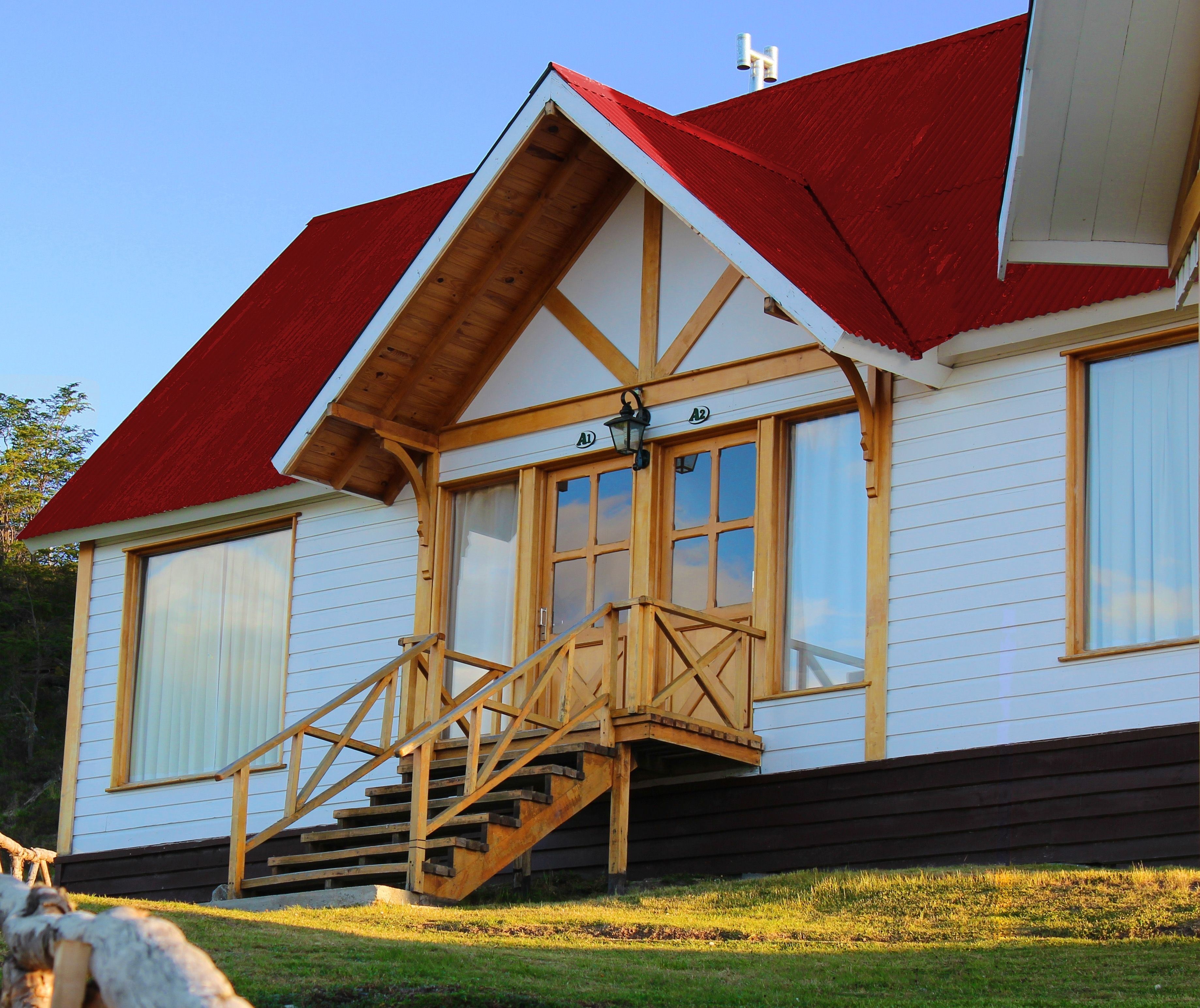 A two-story wooden house with a red roof, a wooden staircase leading to a porch, and a large window on the second floor.