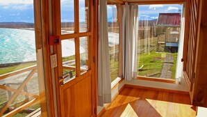 Una habitación con suelo de madera, un ventanal con cortinas y vistas a una playa y un edificio.