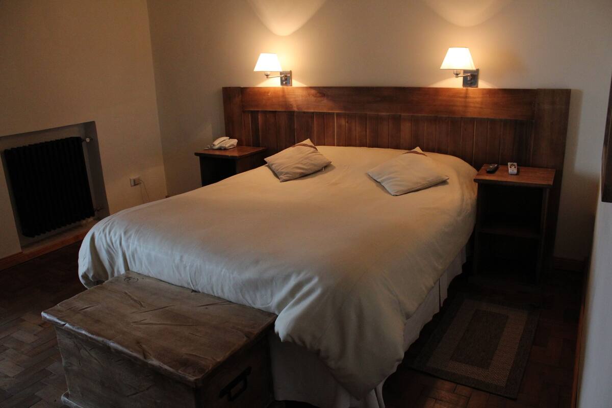 Habitación de hotel con una cama grande, dos mesitas de noche con lámparas, un aparador y un radiador.