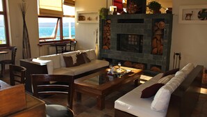 Una sala de estar con chimenea, un sofá, una mesa de comedor y vistas al océano.