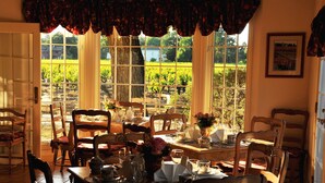 A dining area with a table set for four, surrounded by chairs, with a view of a vineyard through large windows.