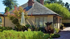 A single-story house with a brick chimney, a covered porch, and a garden with various plants and a pathway leading to the entrance.