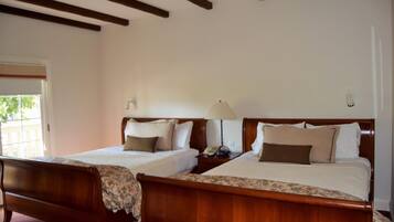 A hotel room with two wooden beds, a nightstand with a lamp, and a window with a view of greenery outside.
