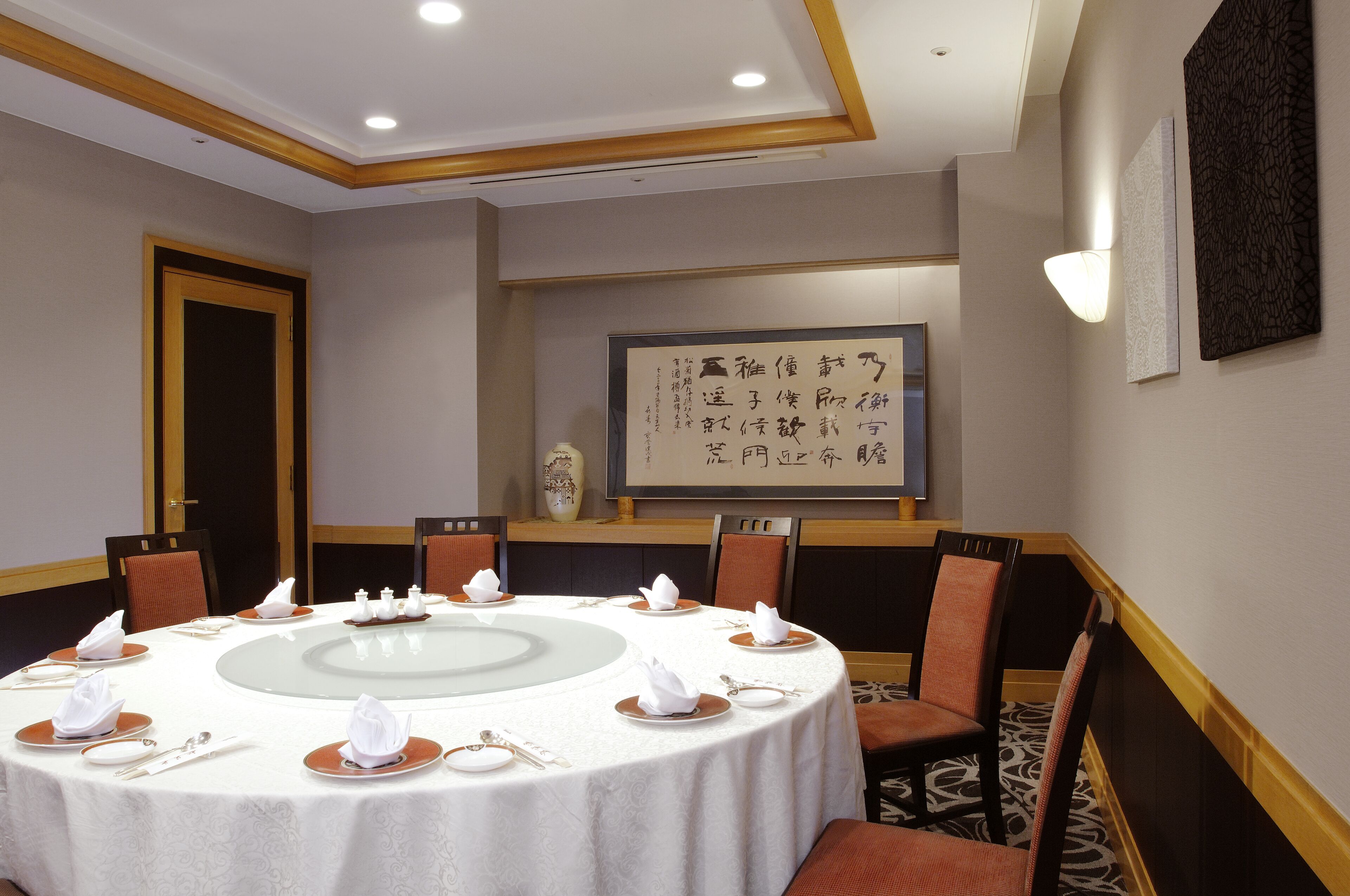 A conference room with a round table, chairs, and a large framed calligraphy piece on the wall.