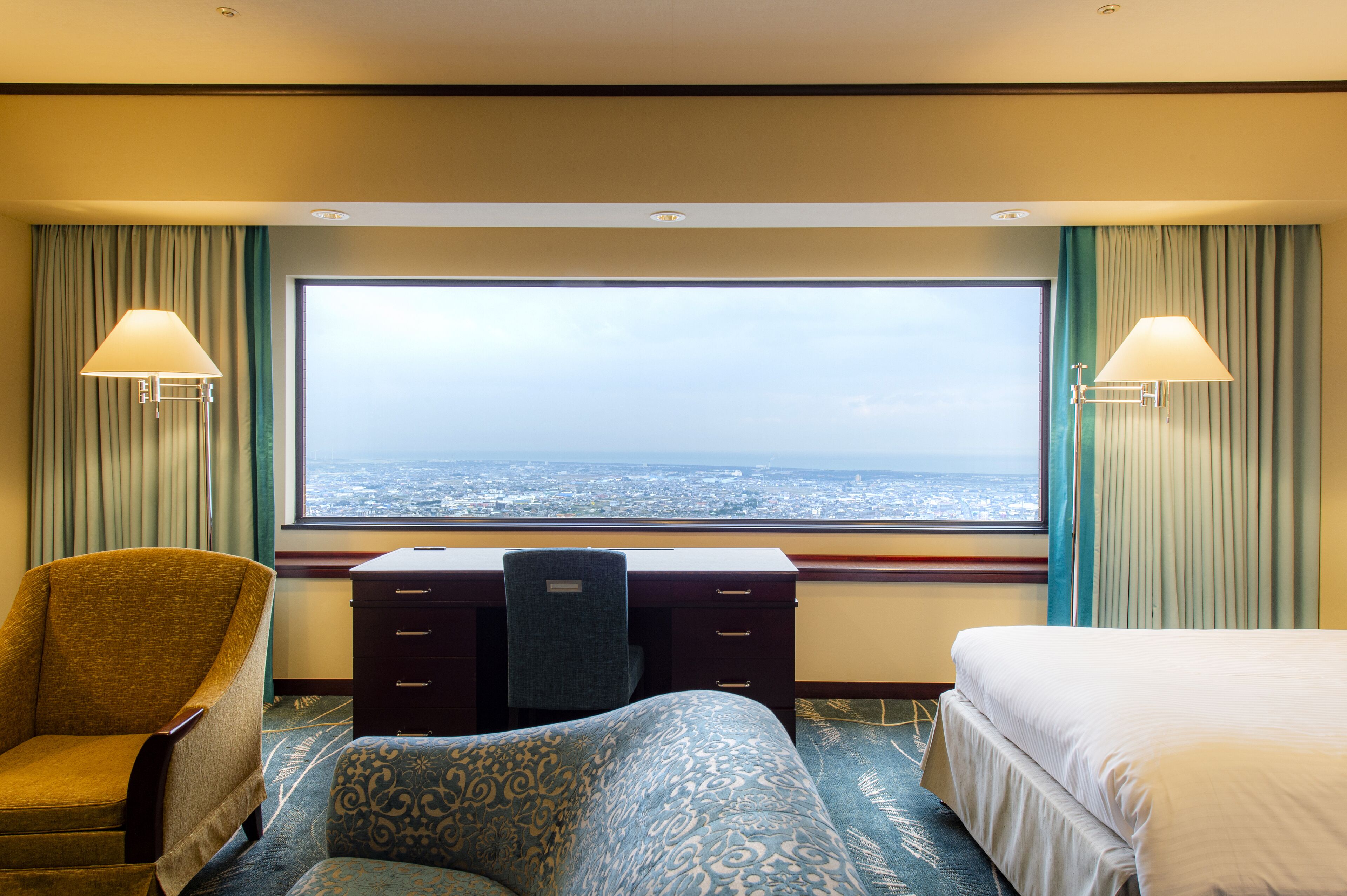 Une chambre d’hôtel avec une grande fenêtre, un bureau, une chaise et un lit.