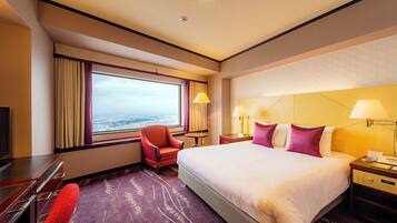 Un cuarto de hotel con una cama grande, un escritorio, una silla y vista a la ciudad a través de la ventana.