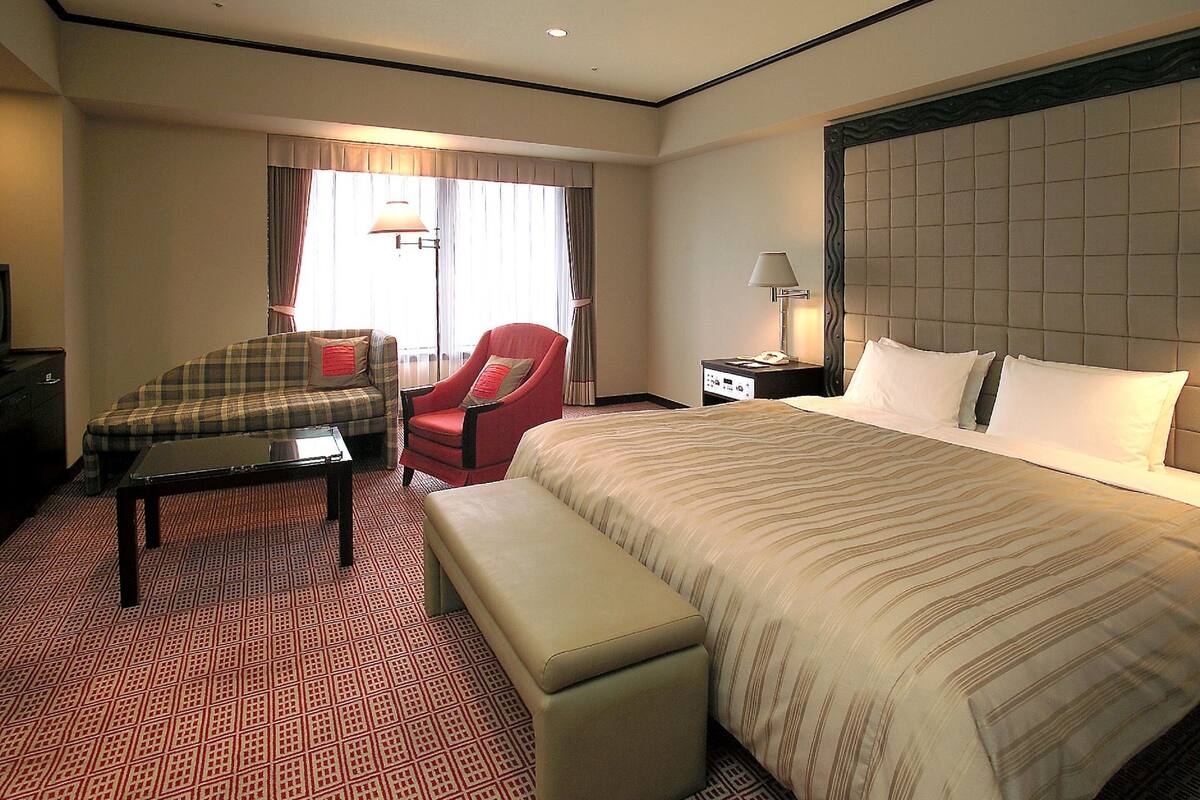 A hotel room with a large bed, a desk, a chair, and a bench.