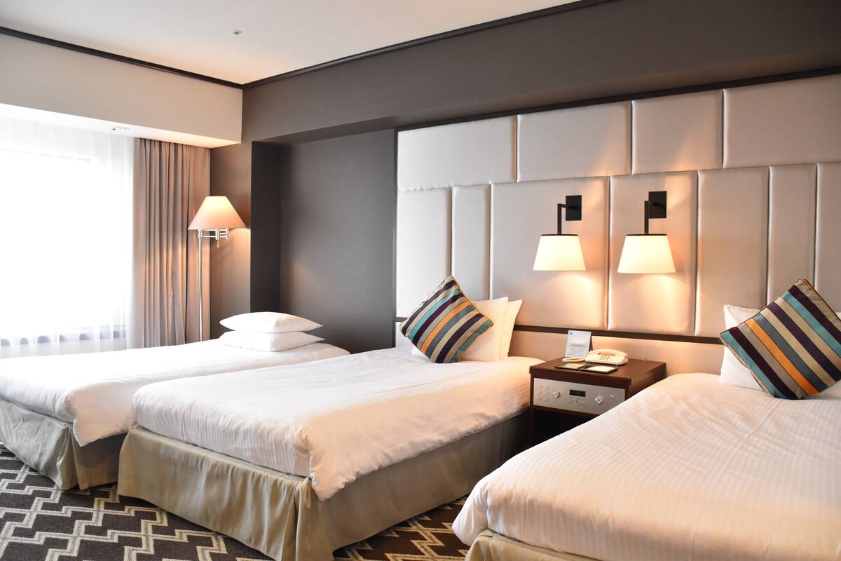 A hotel room with two beds, a nightstand, and a lamp.