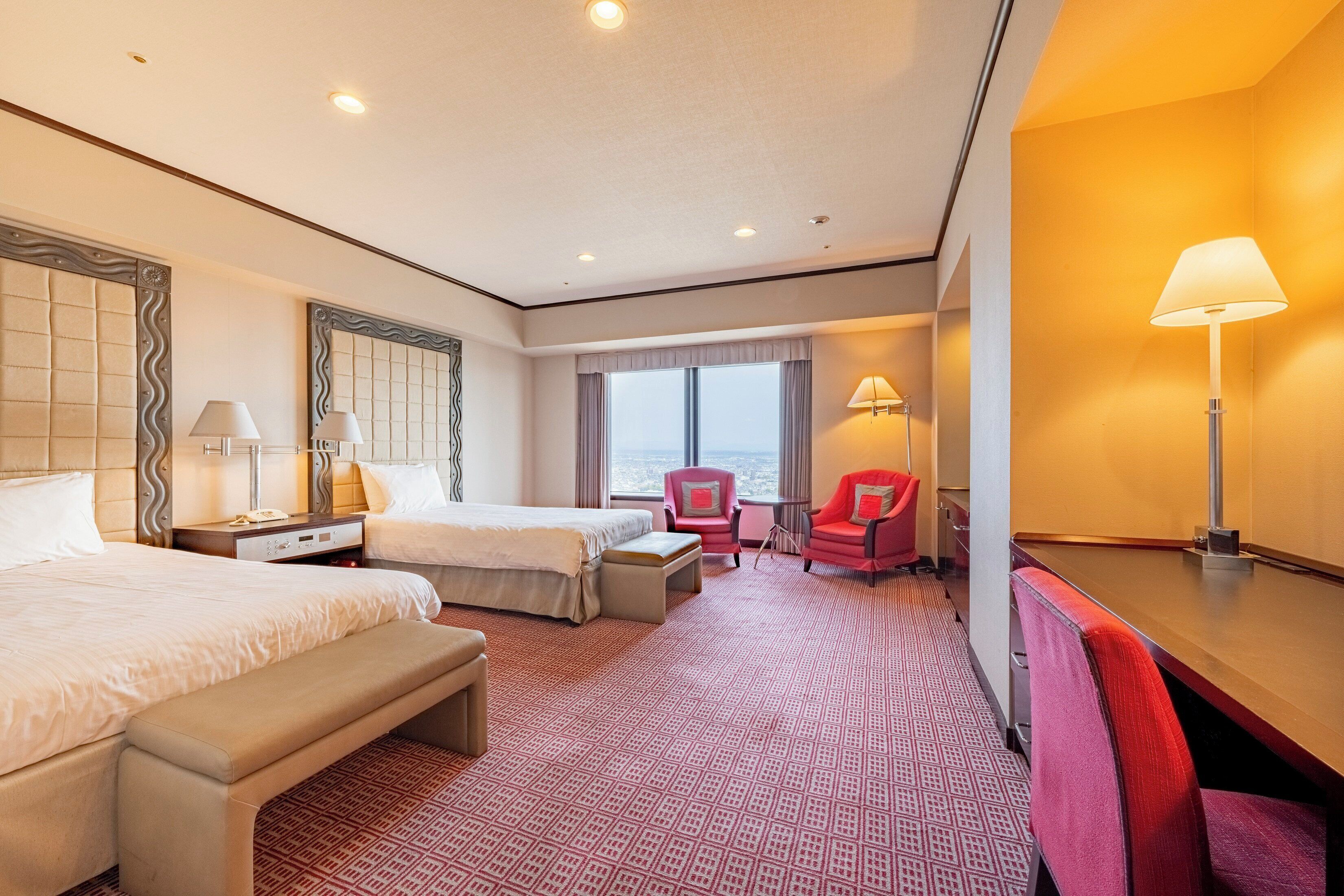 A hotel room with two beds, a desk, a chair, a bench, and a view of the sea.