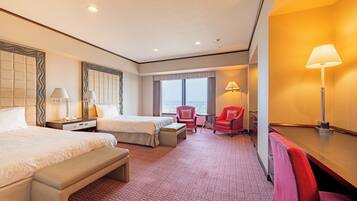 A hotel room with two beds, a desk, a chair, a bench, and a view of the sea.