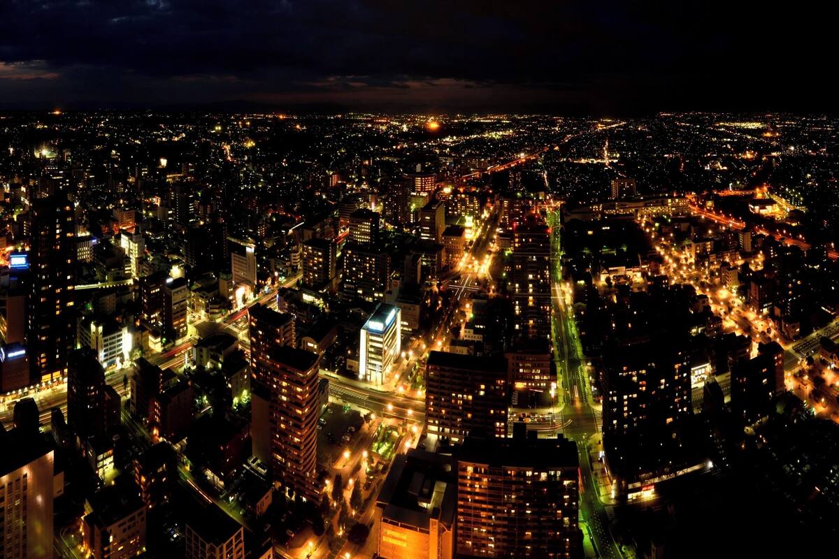 A nighttime aerial view of a densely populated city with illuminated buildings and busy streets.