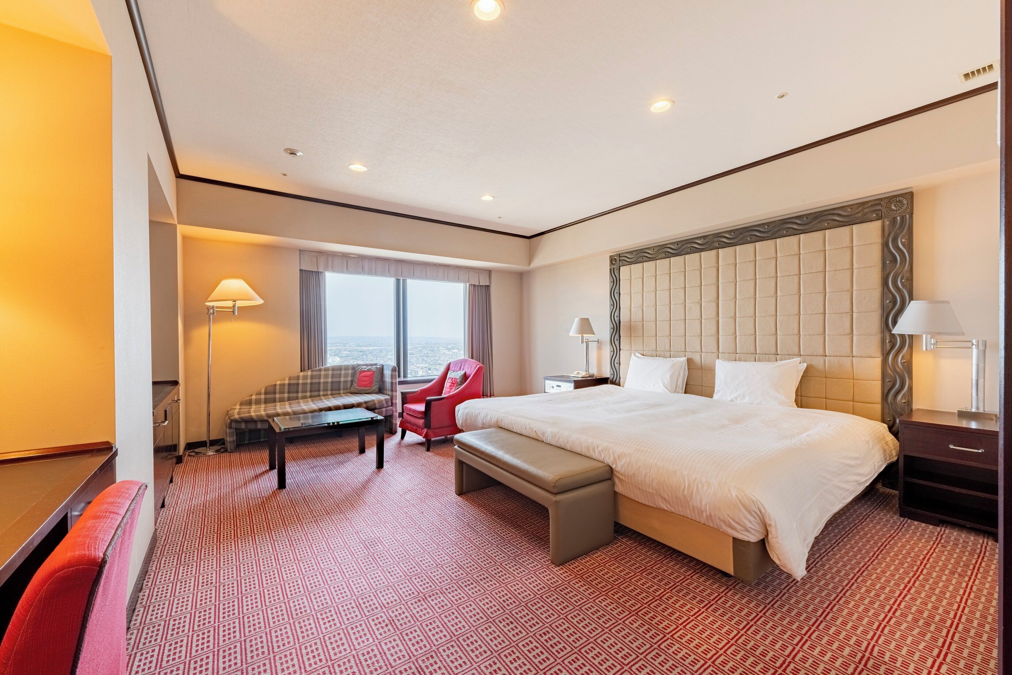 A hotel room with a large bed, a desk, a chair, and a bench.