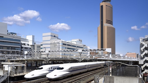 A modern train station with two sleek bullet trains on adjacent tracks, a pedestrian bridge overhead, and a tall building in the background. - Okura Act City Hotel Hamamatsu (Hamamatsu)