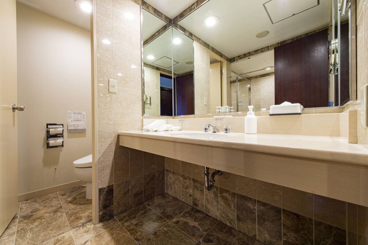 A modern bathroom with a marble sink, a large mirror, and a toilet.