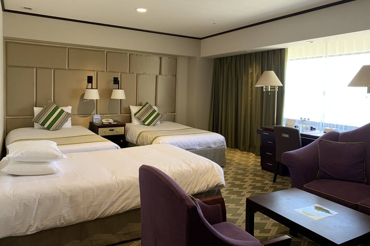 A hotel room with two beds, a desk, a chair, and a couch.