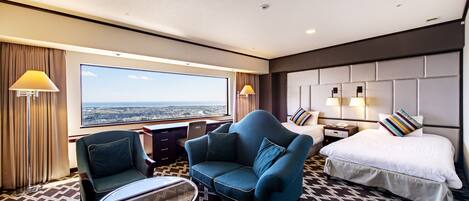 A hotel room with a large window, a sofa, a bed, and a small table.