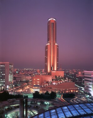 A tall, cylindrical building with a prominent vertical light strip, surrounded by a cityscape at dusk. - Okura Act City Hotel Hamamatsu (Hamamatsu)