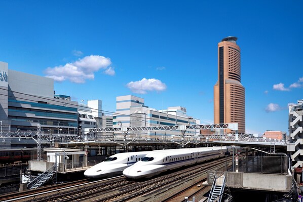A modern train station with two high-speed trains on parallel tracks, a pedestrian bridge, and a tall building in the background. - Okura Act City Hotel Hamamatsu (Hamamatsu)