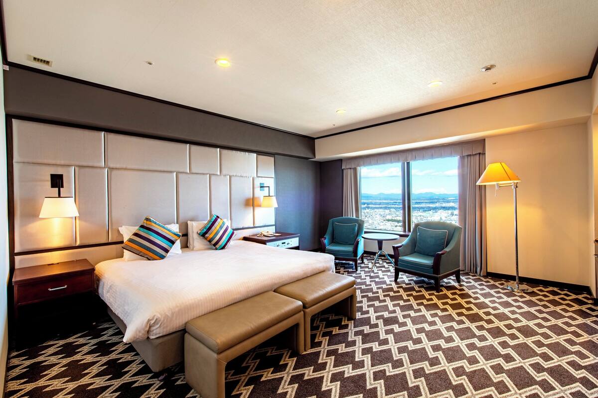 A hotel room with a large bed, a desk, a chair, and a view of the city.
