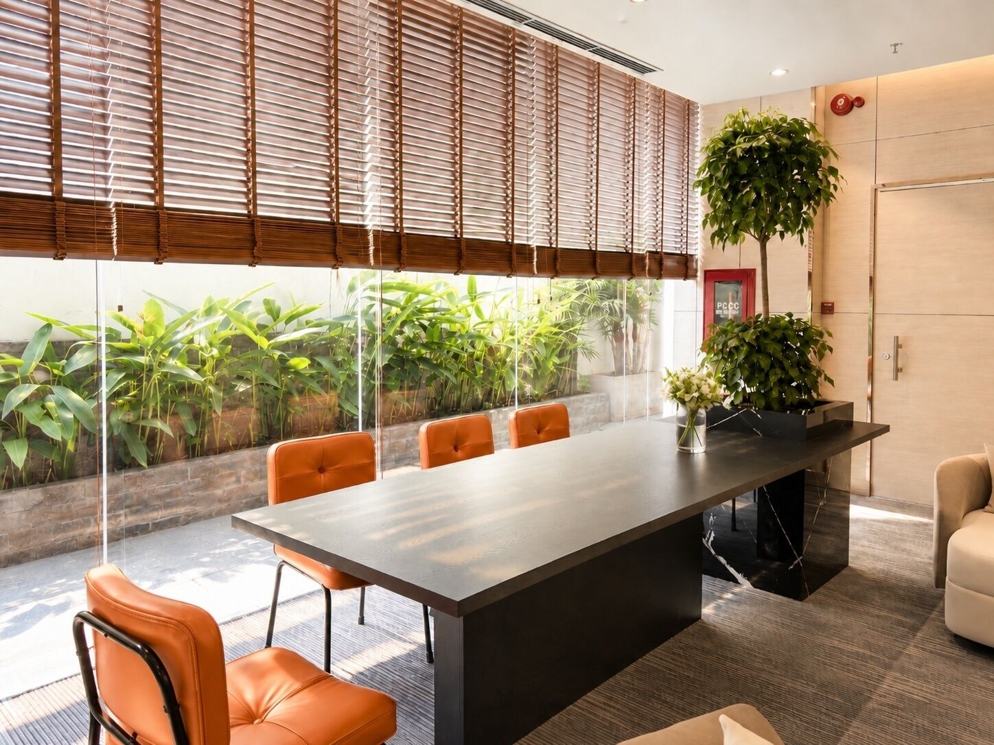 A modern conference room with a large table, four orange chairs, and a potted plant.