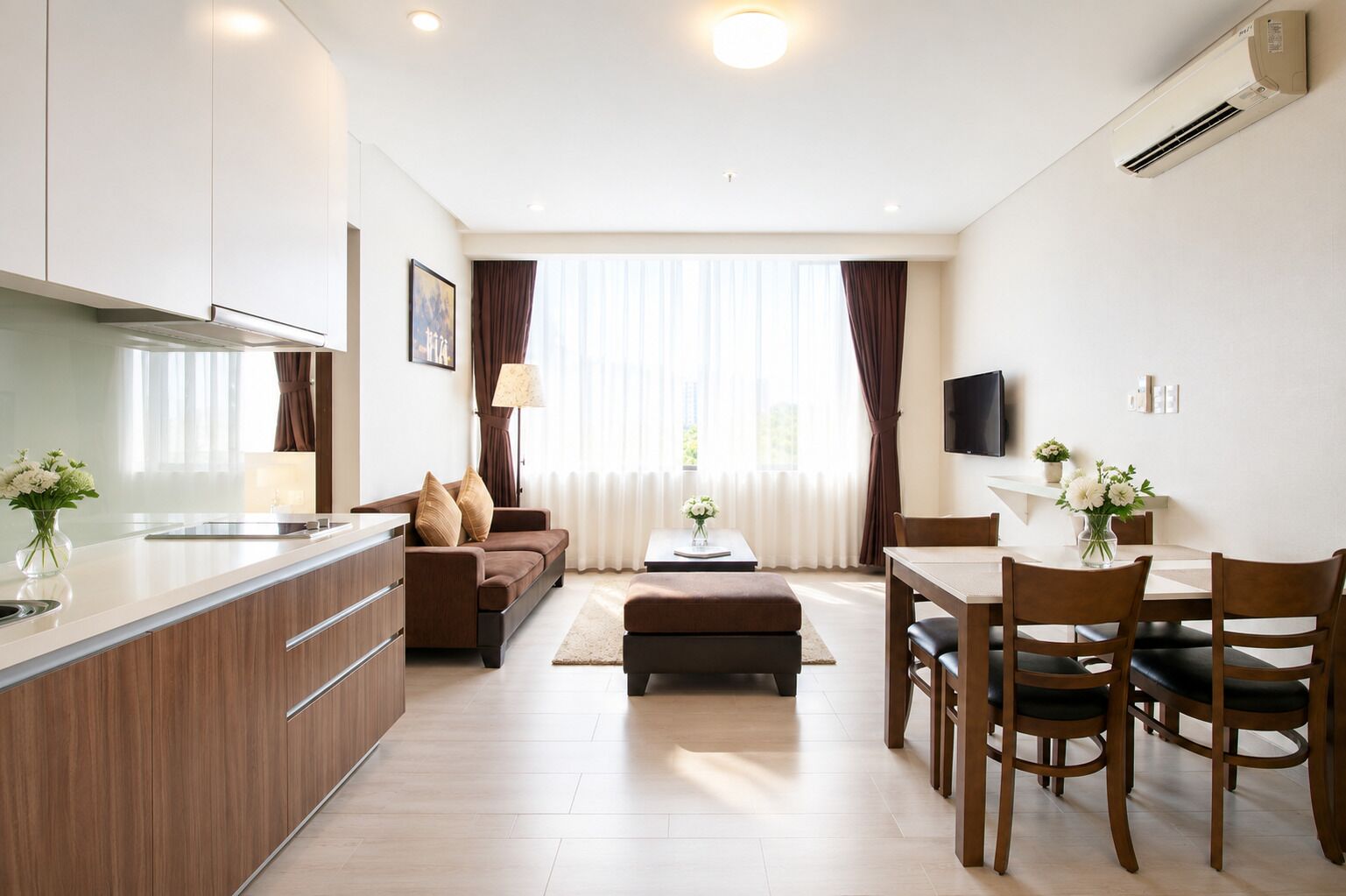 Une cuisine moderne avec un îlot central, un coin repas avec une table et des chaises, un canapé et un téléviseur fixé au mur.