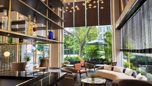 A modern lounge area with seating, a bar with liquor bottles, and large windows offering a view of greenery. - G8 Center Hotel Saigon (Ho Chi Minh City)