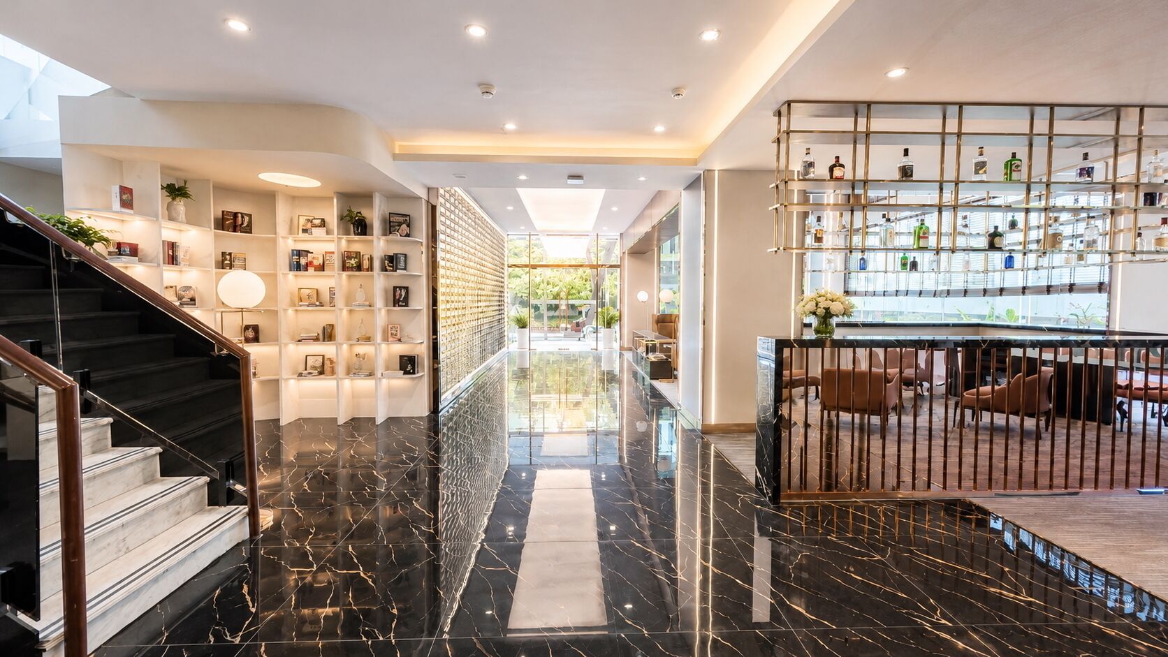 Un hall d’hôtel moderne avec un escalier en marbre, une balustrade en verre et un espace bar.