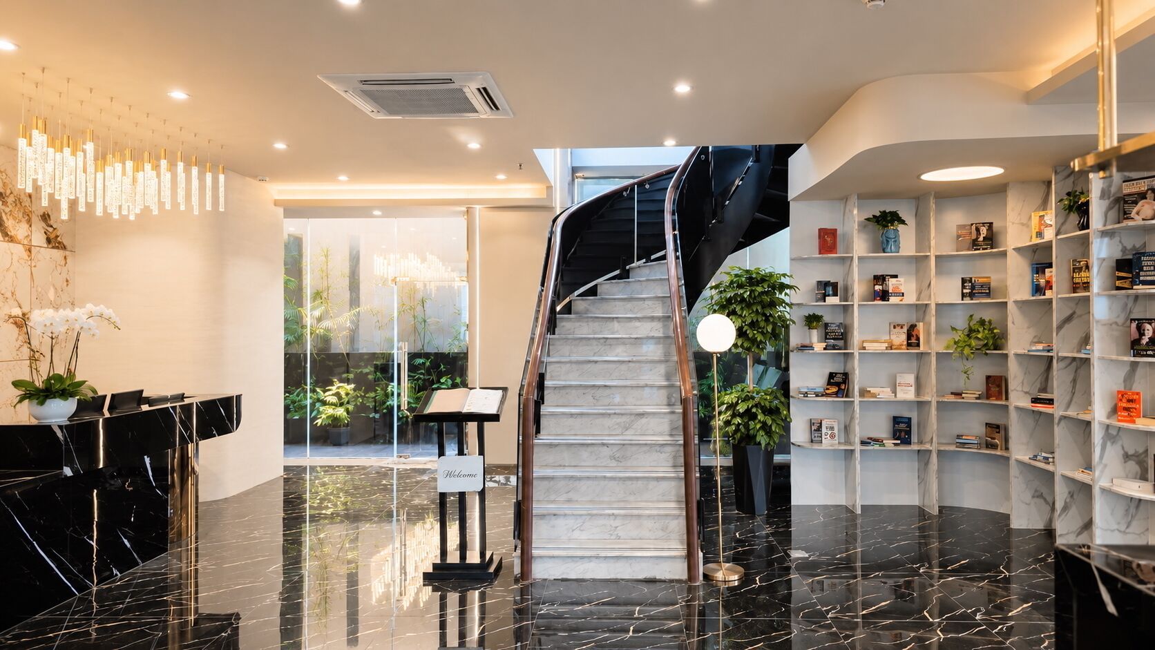 A modern lobby with a marble reception desk, a staircase, and a bookshelf filled with books.