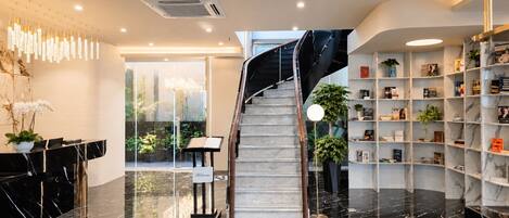 A modern lobby with a marble reception desk, a staircase, and a bookshelf filled with books.