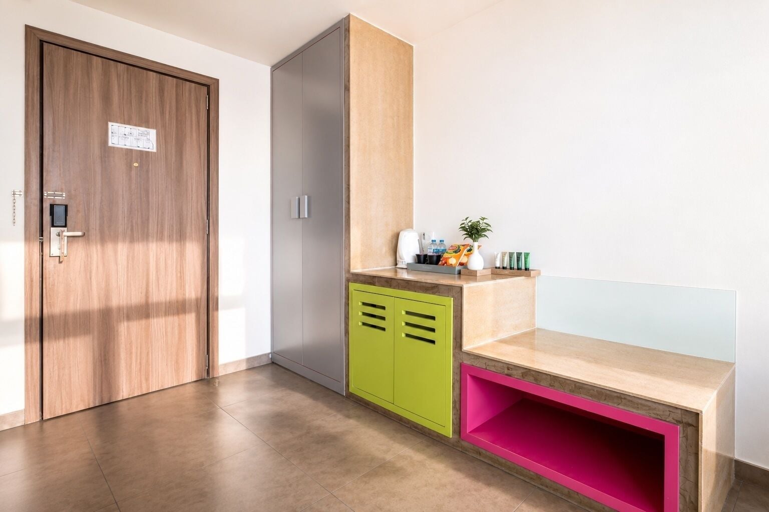 A hotel room with a wooden door, a green and pink cabinet, and a beige countertop.