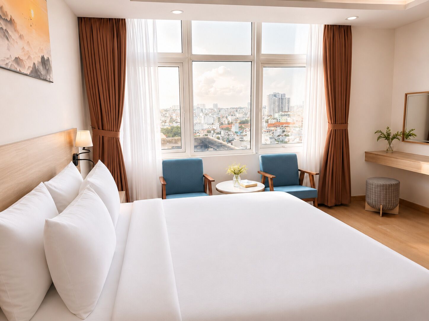 Ein Hotelzimmer mit einem großen Bett, zwei Sesseln, einem kleinen Tisch und Blick auf eine Stadtlandschaft durch große Fenster.