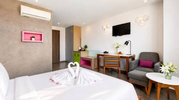 Quarto de hotel com cama, escrivaninha, cadeira, televisão e uma pequena mesa com flores.