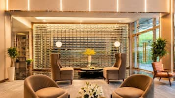 A lobby with two armchairs, a round table with a vase of flowers, a decorative wall, and a bookshelf.