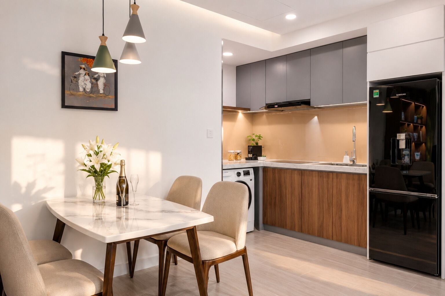A modern kitchen with a dining area, featuring a marble table, pendant lights, and a refrigerator.
