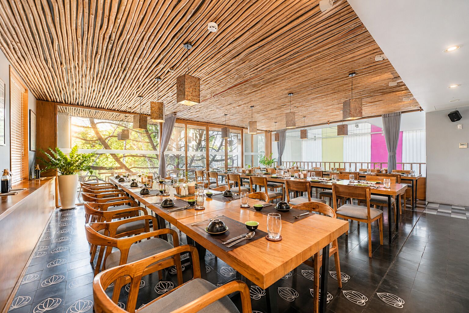 Un restaurante con mesas y sillas de madera, ventanas grandes y un techo con listones de madera.