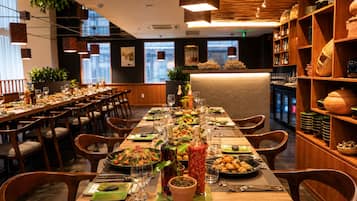 A restaurant with long communal tables, wooden chairs, and shelves with kitchenware.