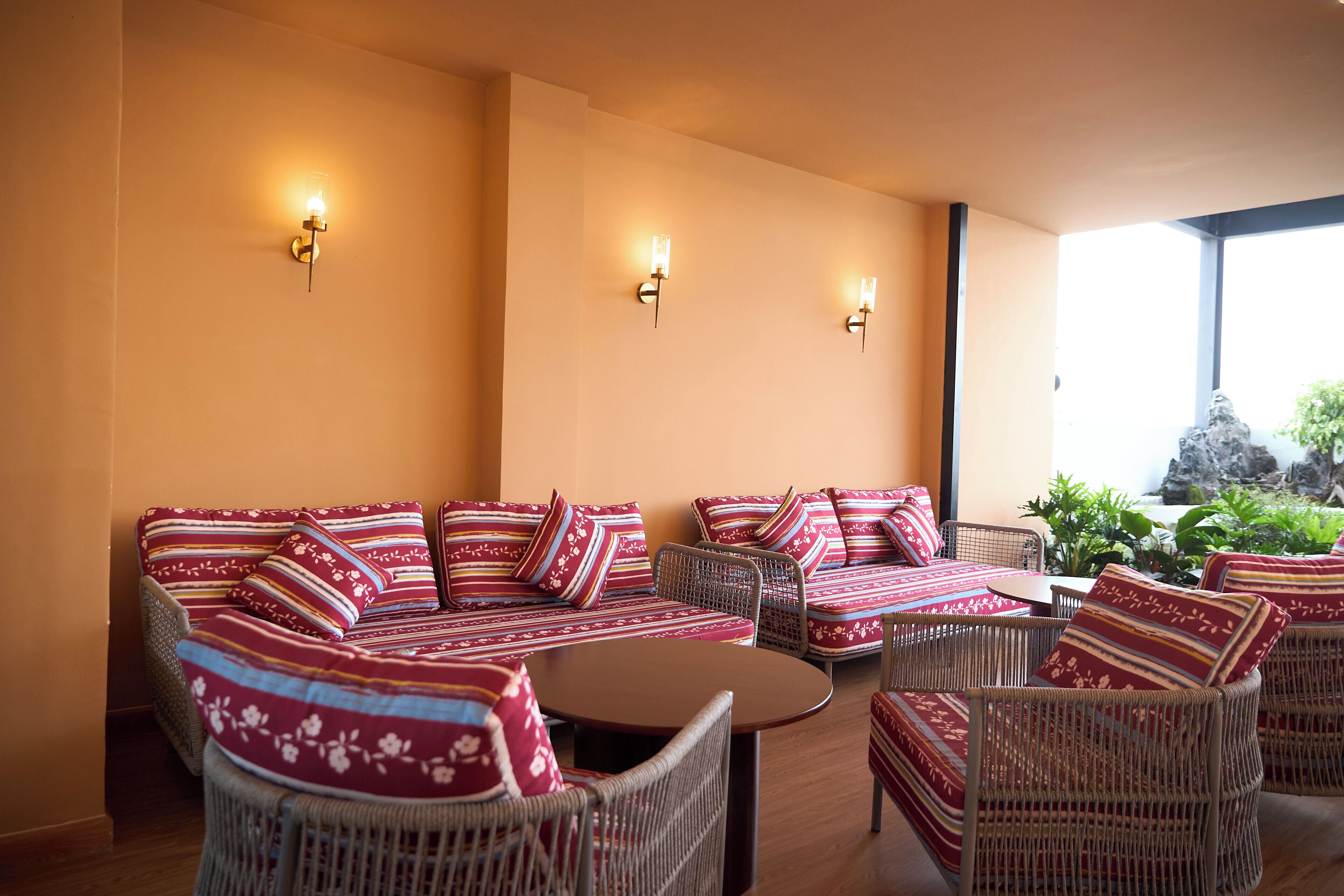 A room with a sofa set, wicker chairs, a round table, and wall-mounted lights.