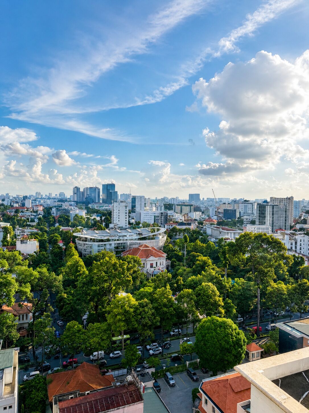 A cityscape with a mix of modern and traditional architecture, a prominent curved building, and a dense tree-lined area.