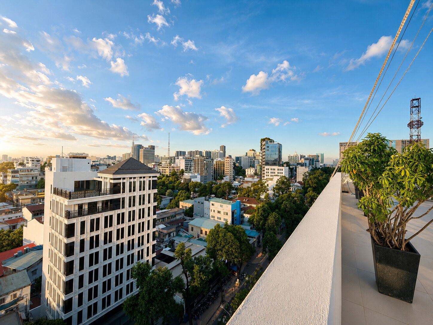 Stadsgezicht met moderne gebouwen, een heldere lucht en een plant in een pot op een balkon.