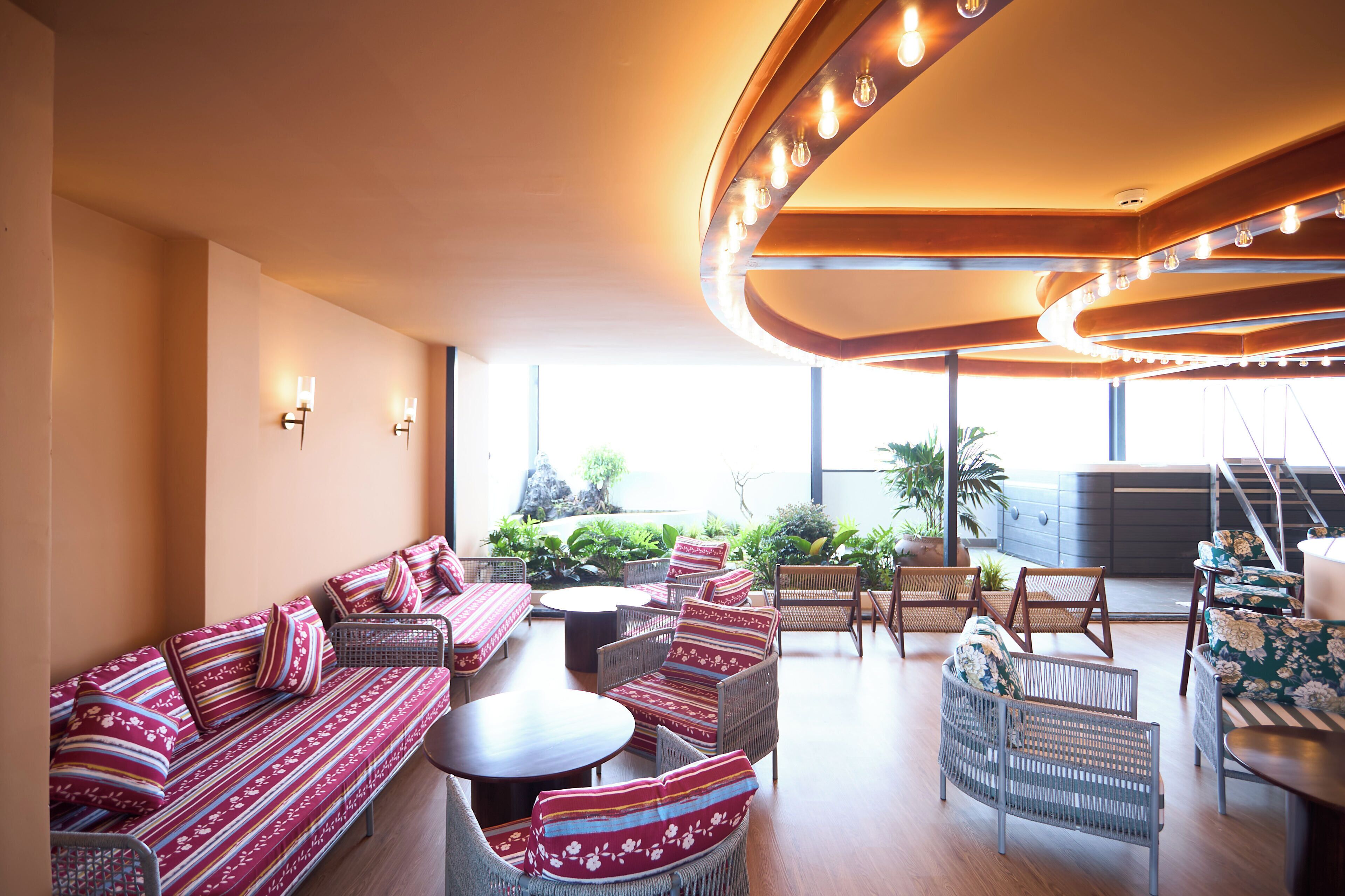 A spacious indoor area with seating arrangements, a staircase, and large windows.