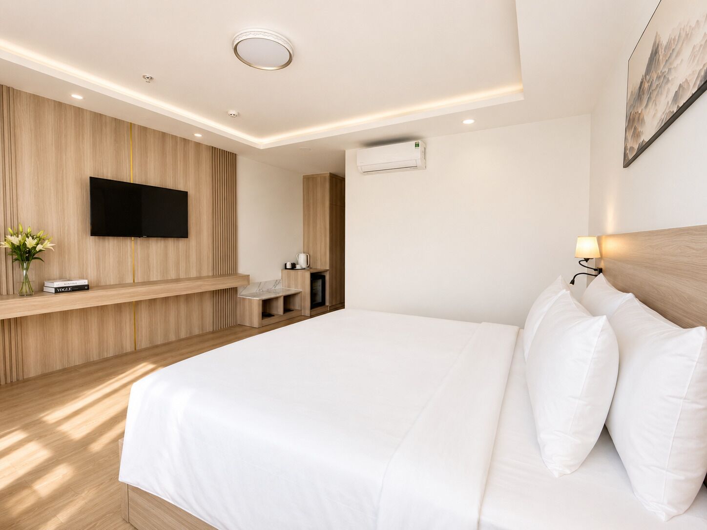 Una habitación de hotel moderna con una cama grande, un televisor de pantalla plana montado en una pared de madera, una pequeña zona de estar y un equipo de aire acondicionado instalado en la pared.