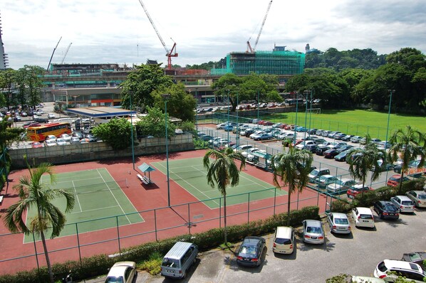 A parking lot with multiple cars and a tennis court.