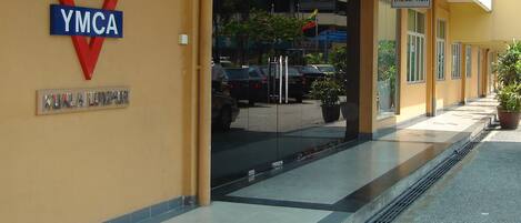 Entrada de un edificio con un cartel que dice 'Welcome to YMCA', una zona de recepción y un estacionamiento con coches.