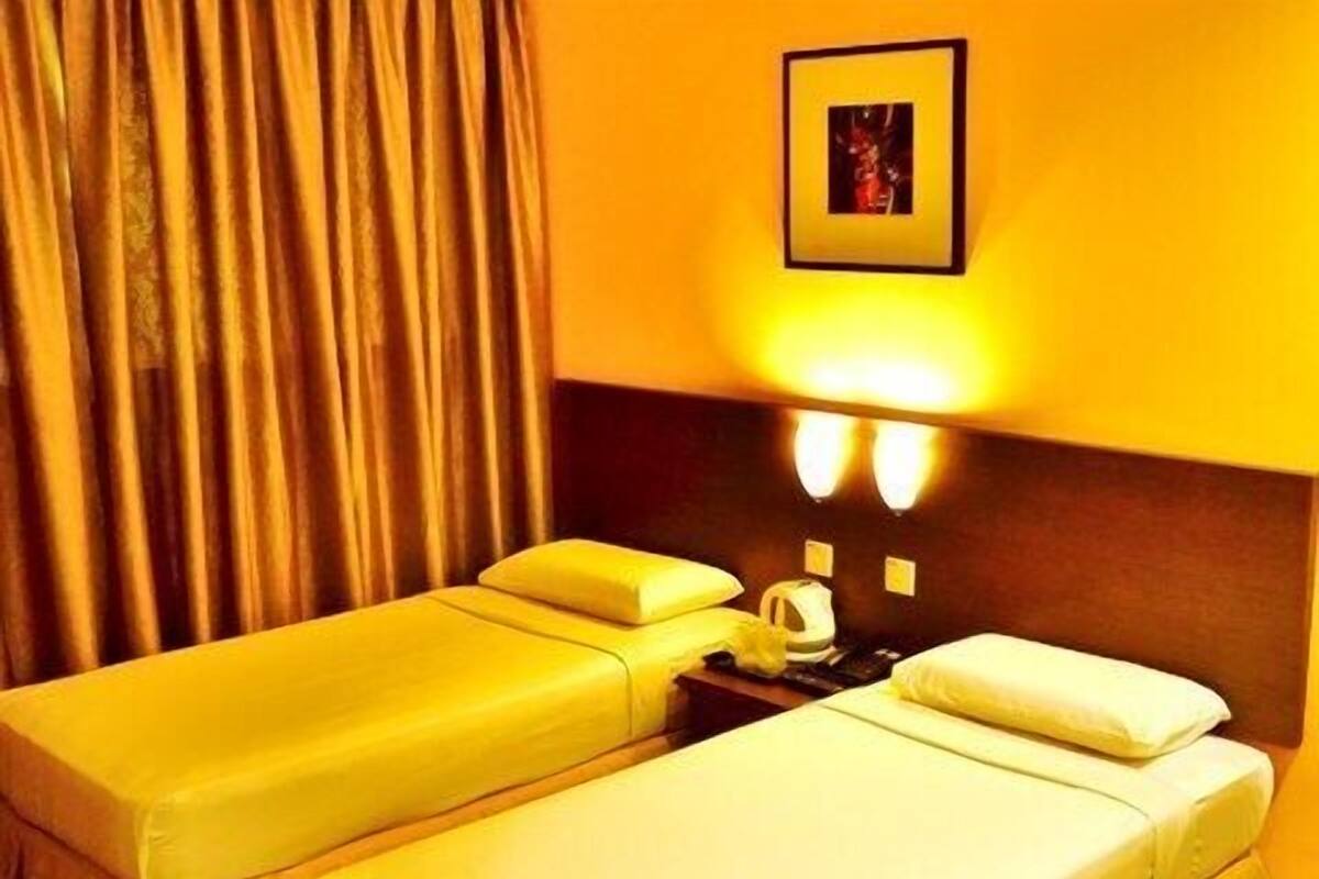 A hotel room with two single beds, a nightstand with a lamp, and a framed picture on the wall.
