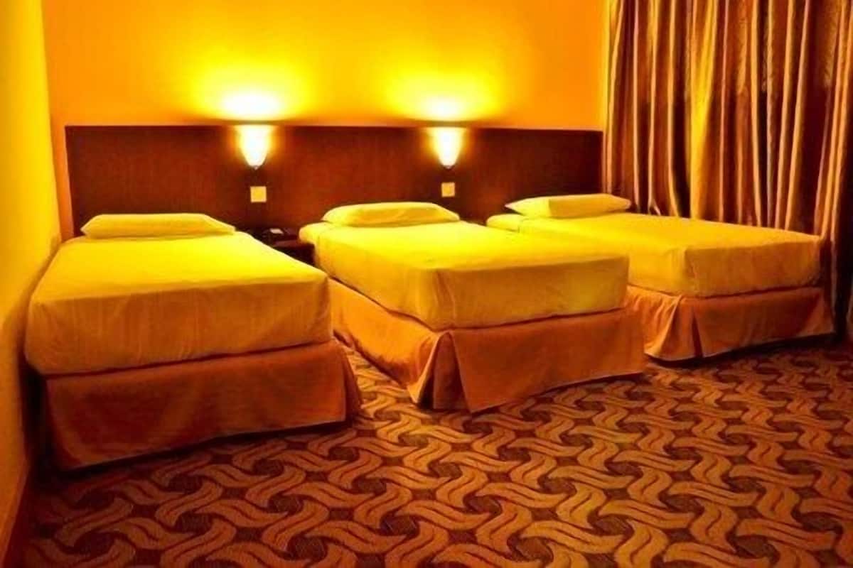 A hotel room with three single beds, a patterned carpet, and two wall-mounted lights.