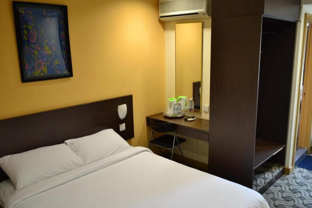 A hotel room with a bed, a desk, a chair, a mirror, and an air conditioning unit.