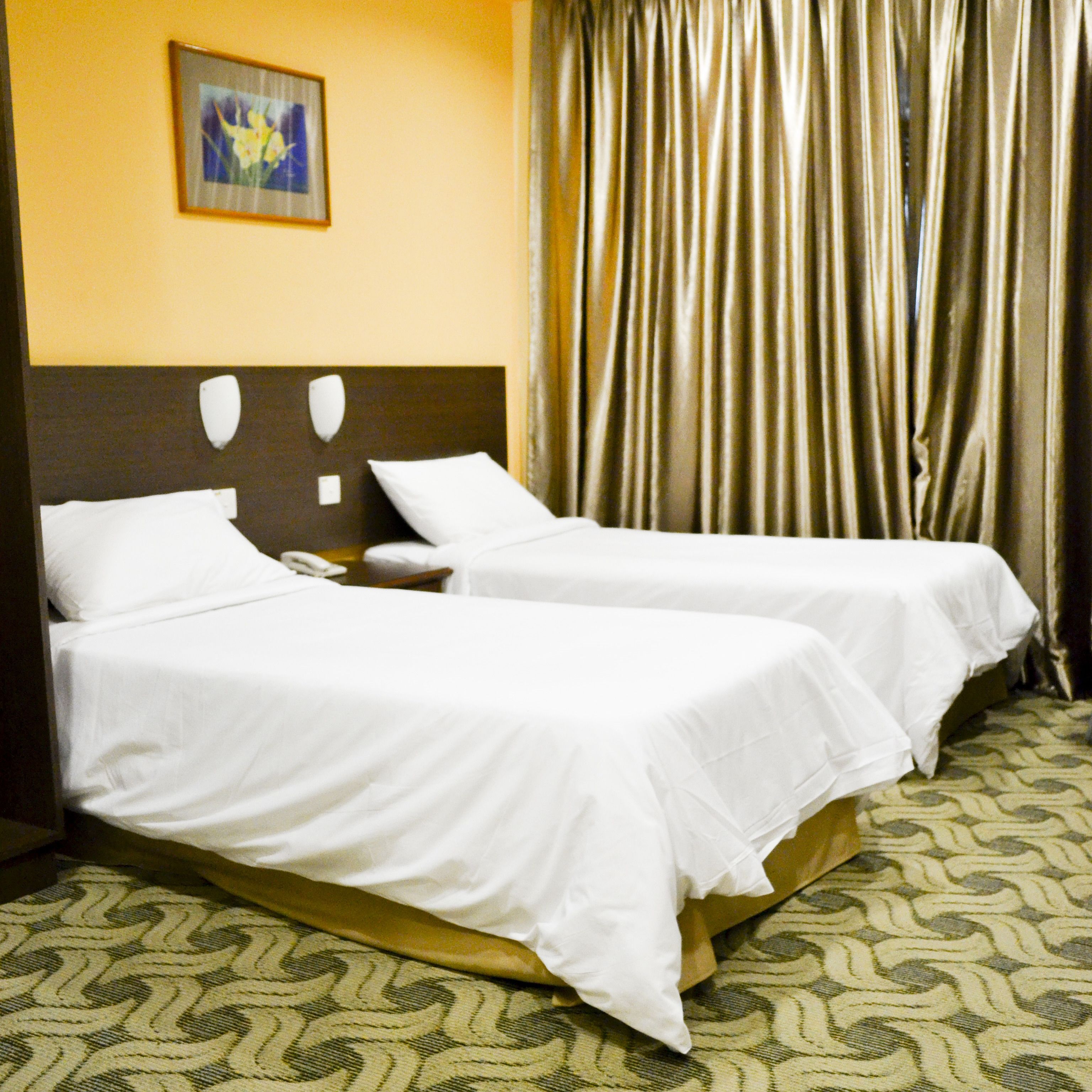 A hotel room with two single beds, a nightstand with a phone, a painting on the wall, and a curtain.