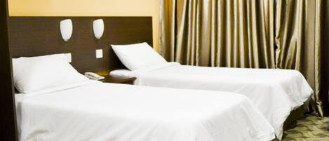 A hotel room with two single beds, a nightstand with a phone, a painting on the wall, and a curtain.